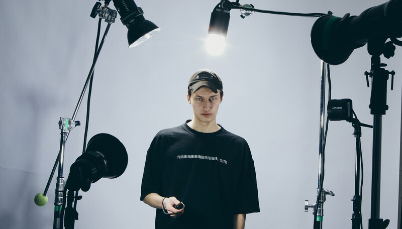 Young man in black t-shirt and cap standing in studio surrounded by professional lighting equipment.