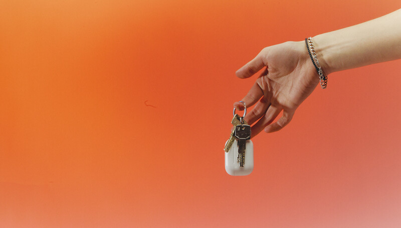 Hand holding a keychain with keys against a warm orange gradient background.