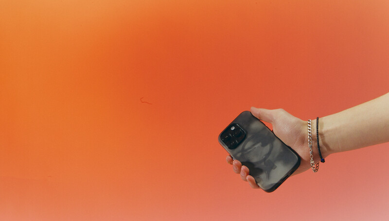 Hand holding a smartphone with a cracked screen against an orange gradient background.