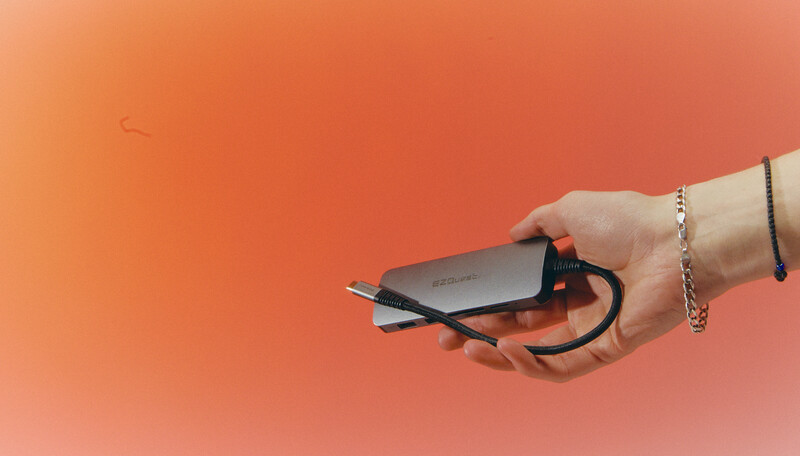 Hand holding a portable external hard drive against a warm coral-orange gradient background.