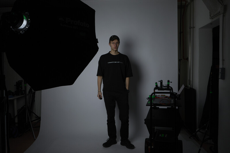 Photographer standing in studio setup with large softbox and lighting equipment visible.