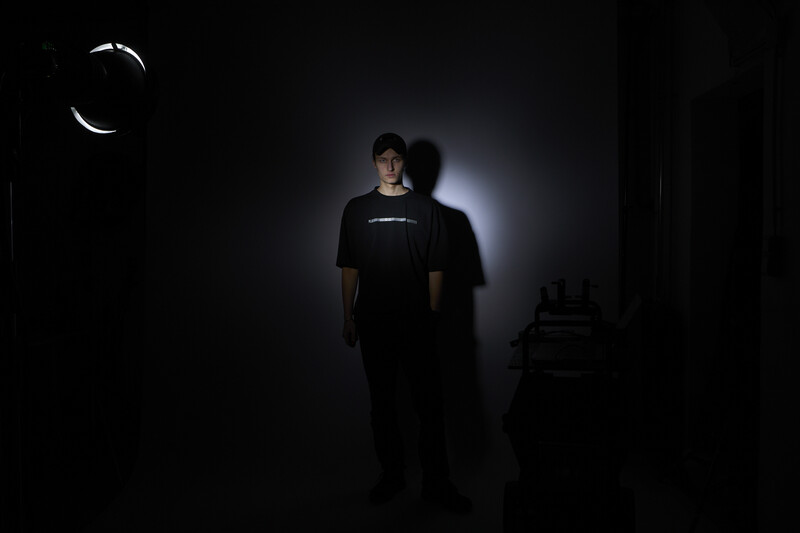 Person in black t-shirt illuminated by dramatic backlit glow against dark background.