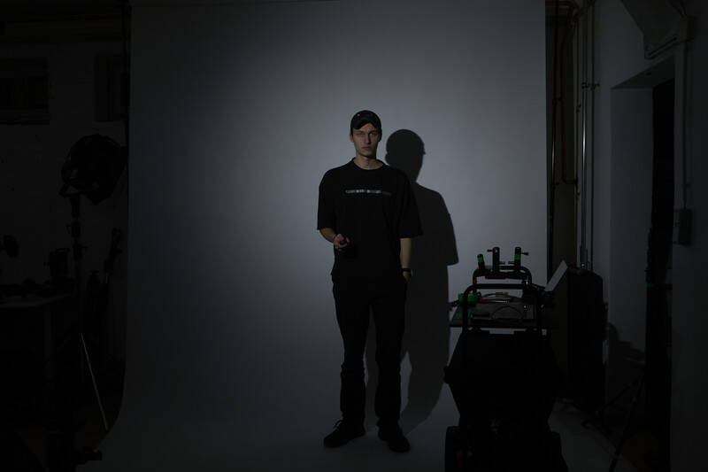 Person in black clothing standing against illuminated white backdrop in studio setting.