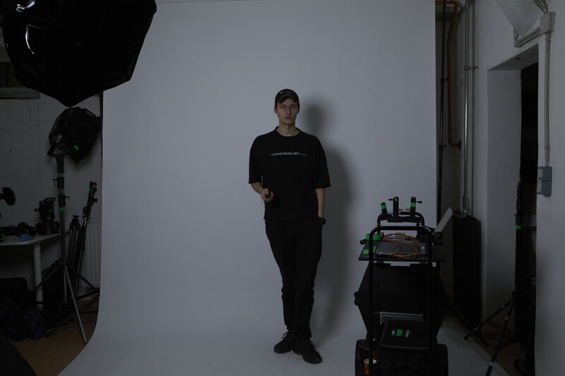 Studio portrait setup with subject in black clothing against white backdrop and professional lighting equipment visible.
