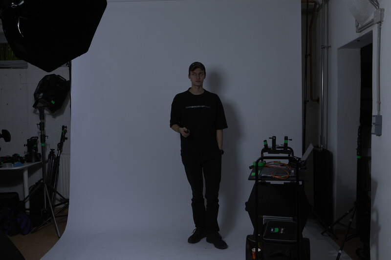 Photographer standing against white backdrop in studio with professional lighting equipment visible on either side.
