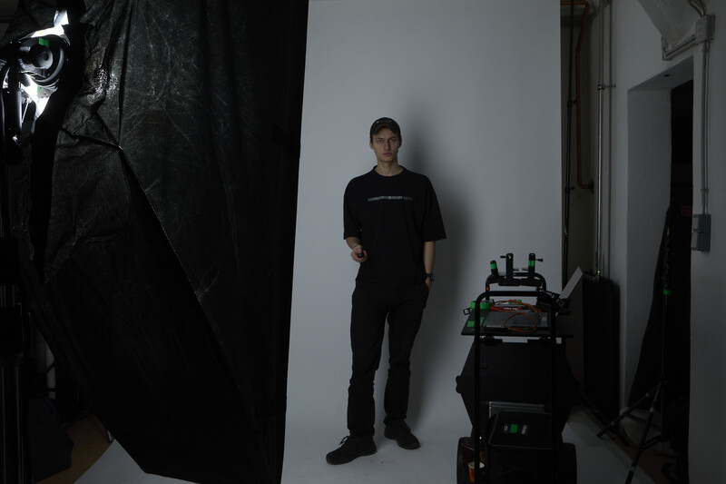 Man standing against white wall in studio setup with professional lighting equipment and black fabric reflectors.