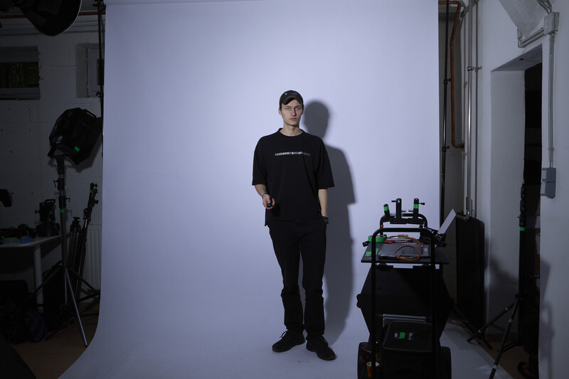 Person in black clothing standing against white cyclorama in studio with professional lighting equipment visible.