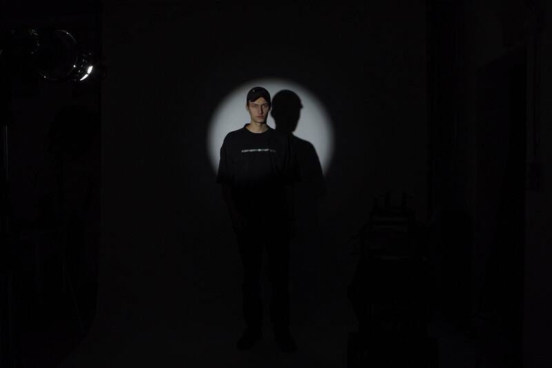 Two silhouetted figures standing against a bright backlit glow in darkness.