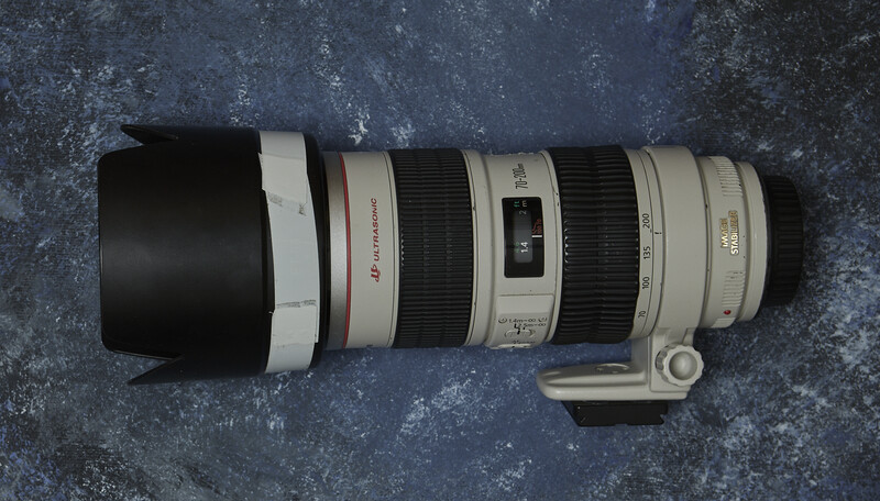 Canon telephoto zoom lens with white barrel and black rubber grip mounted on textured gray surface.