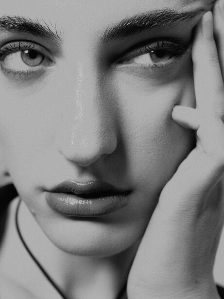 Black and white portrait of a person with hand raised to face, direct gaze at camera.