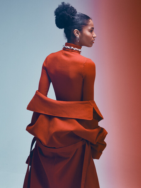 Woman in rust-colored ruffled dress photographed against gradient blue-to-red background.