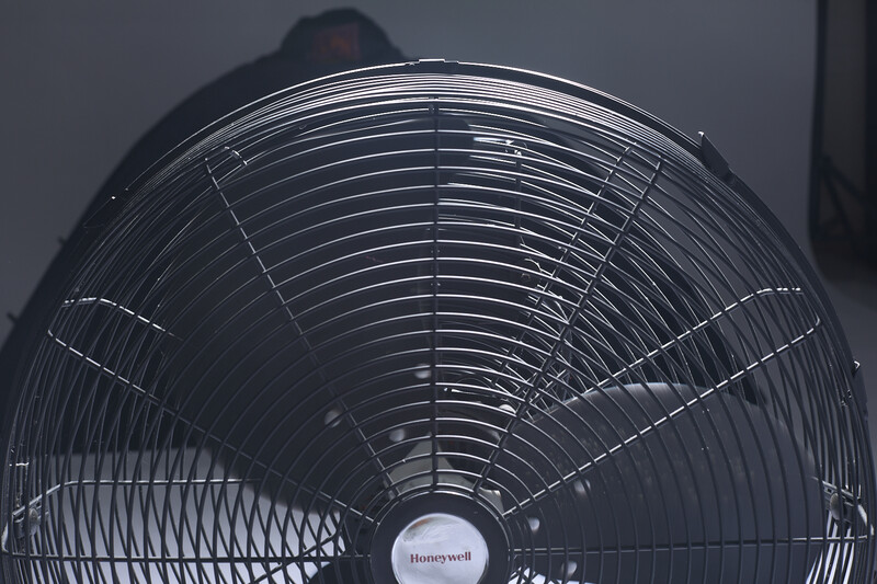 Close-up front view of an electric fan with metal grilles and visible motor housing against a neutral background.