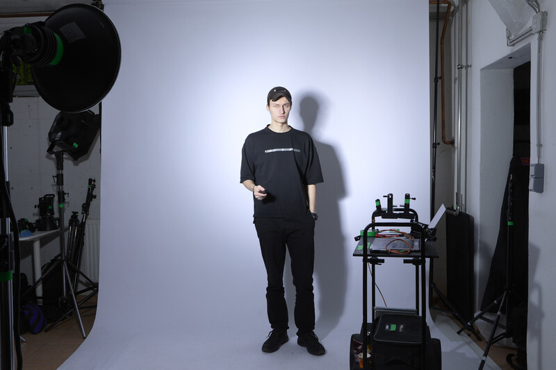 Man in black clothing standing in a professional studio setup with controlled lighting.