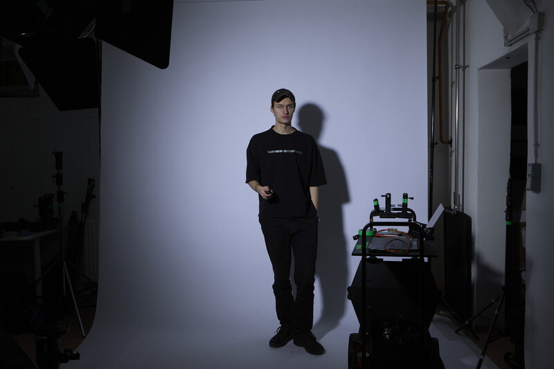 Man in black shirt standing against white cyclorama backdrop in studio with professional lighting setup.