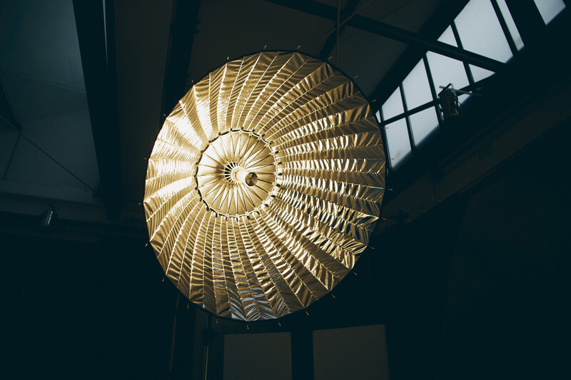 Golden spiral pendant lamp with radiating geometric pattern suspended from dark ceiling.