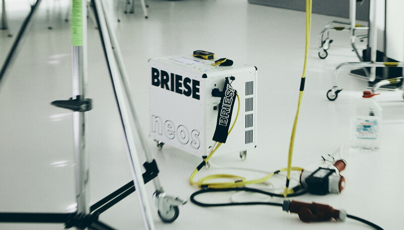 Overhead view of a white equipment case labeled BRIESE with cables and studio gear scattered on a white floor.