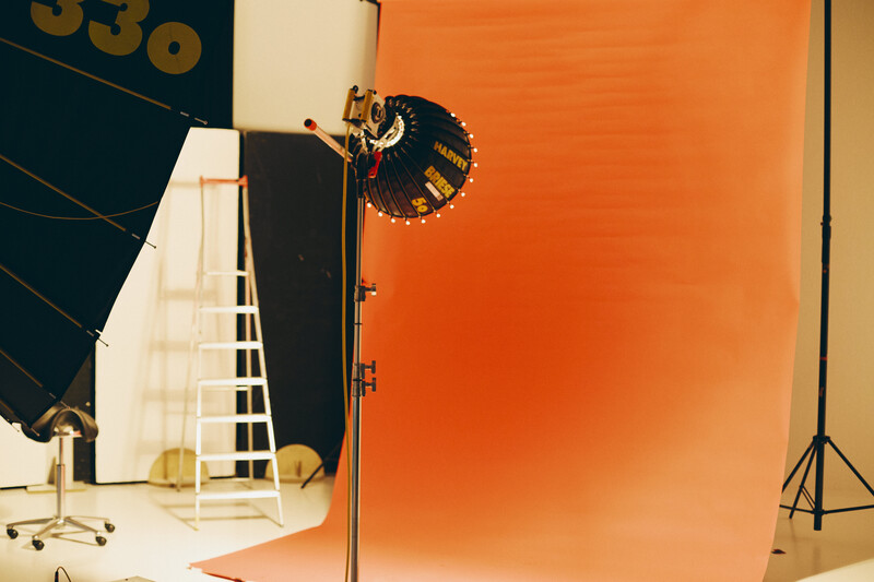 Professional studio setup with orange seamless backdrop, key light with reflector, and lighting stand.