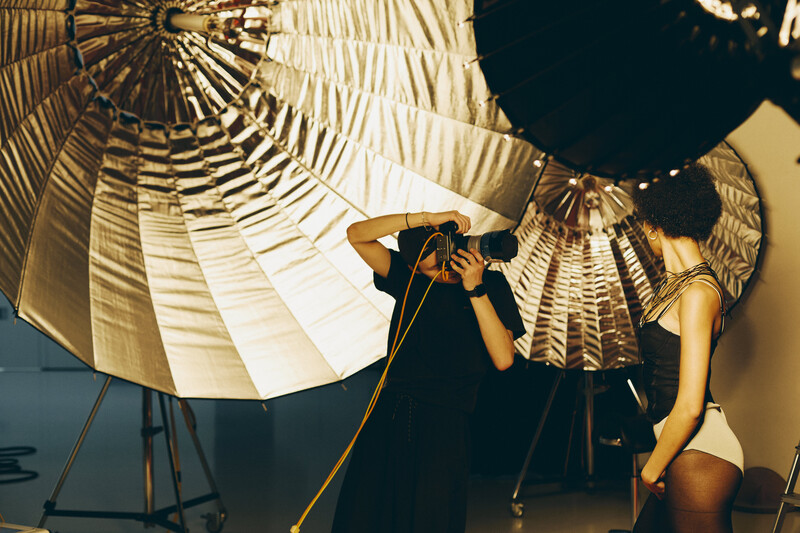 Photographer adjusting lighting setup with large reflective umbrellas in studio.