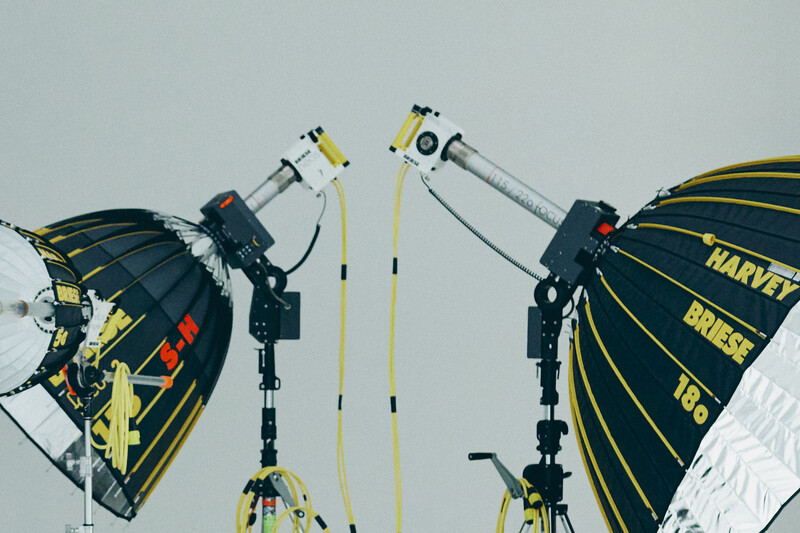 Professional lighting setup with two large parabolic umbrellas mounted on overhead rigging equipment against a white sky.
