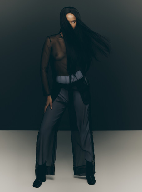 Person in dark clothing posed against neutral background with dramatic side lighting.