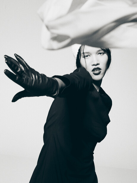 Person in black outfit with dramatic makeup and flowing white fabric against neutral background.