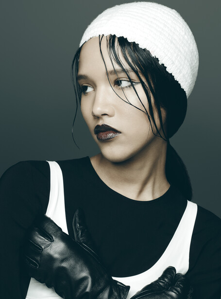 Portrait of a person with dramatic makeup and styled black hair partially covered by a white knit beanie.