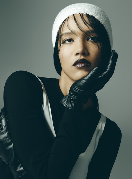 Portrait of a person wearing a white beanie and black gloves against a neutral gray background.