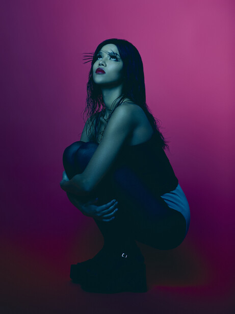 Woman with long dark hair gazes upward against a vibrant magenta background.