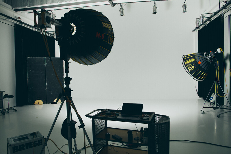 Professional studio setup with large softbox key light on left, fill light on right, and laptop on desk in center of white seamless backdrop.
