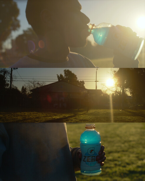 Turquoise beverage bottle backlit by golden sunset with silhouetted person and landscape in background.