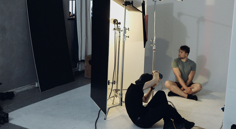 Behind-the-scenes studio setup showing two people during a photo shoot with professional lighting stands and black reflector panels.