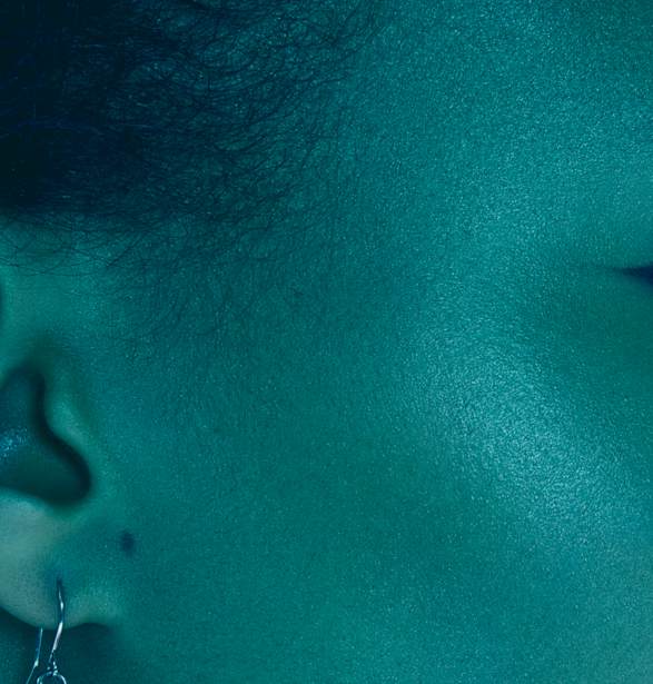Close-up of a person's face in profile against a teal-tinted, textured background with bokeh effects.