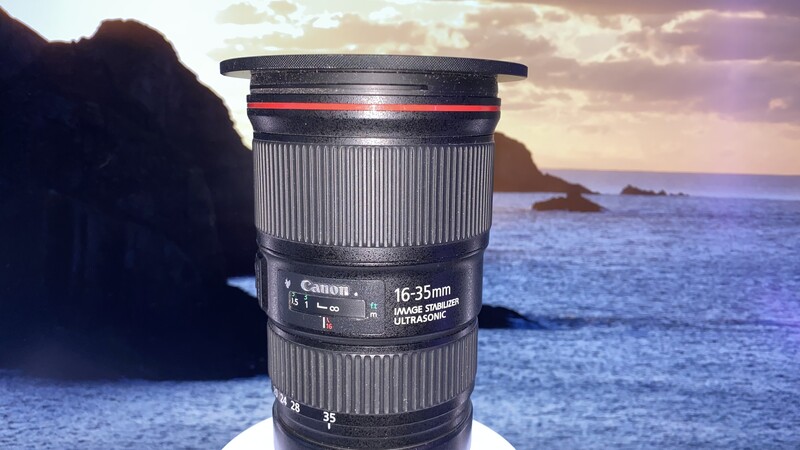 Canon 16-35mm telephoto zoom lens positioned against a coastal seascape backdrop.