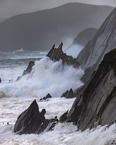 Dramatic coastal seascape with jagged rock formations and crashing waves against stormy skies