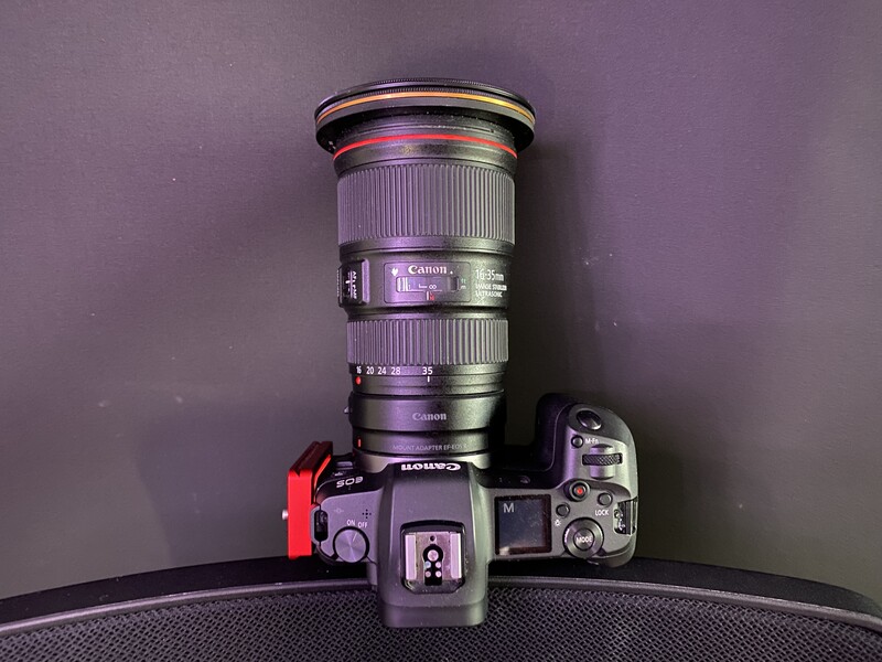 Mirrorless camera with large telephoto lens mounted, displayed against purple background with dramatic side lighting.