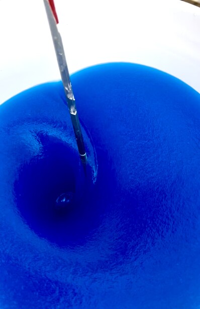 Paintbrush with blue bristles painting deep blue acrylic or gouache on a spherical surface.
