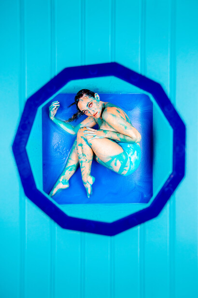 Aerial view of a person floating in a bright blue swimming pool within a geometric octagonal frame.