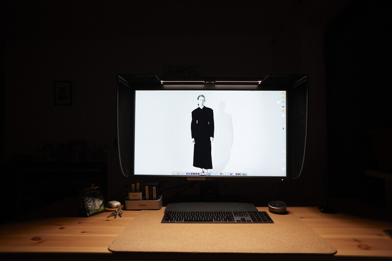 Computer monitor on wooden desk displaying a figure in black clothing against white background in dark room.