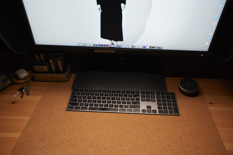 Overhead view of a workspace with a monitor, wireless keyboard, and mouse on a cork desk pad.