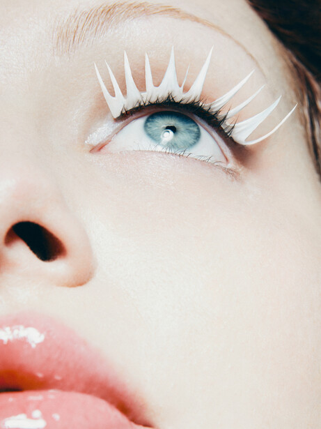Close-up beauty portrait of a woman's eye with pale eyeshadow, defined eyeliner, and white false lashes.