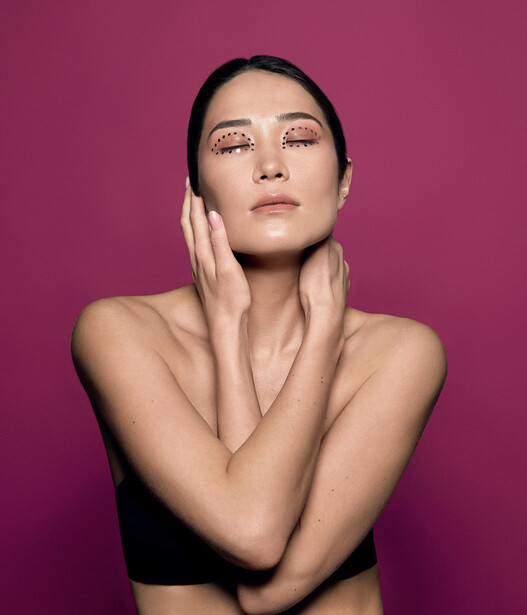 Woman with dark hair gazing upward against vibrant magenta background with hands framing face.
