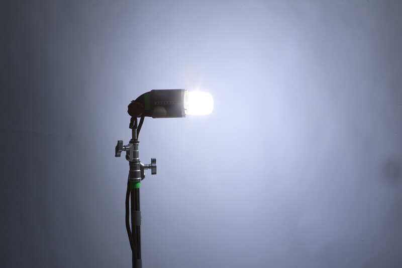 Studio flash head mounted on a stand, brightly illuminated against a gray overcast sky.