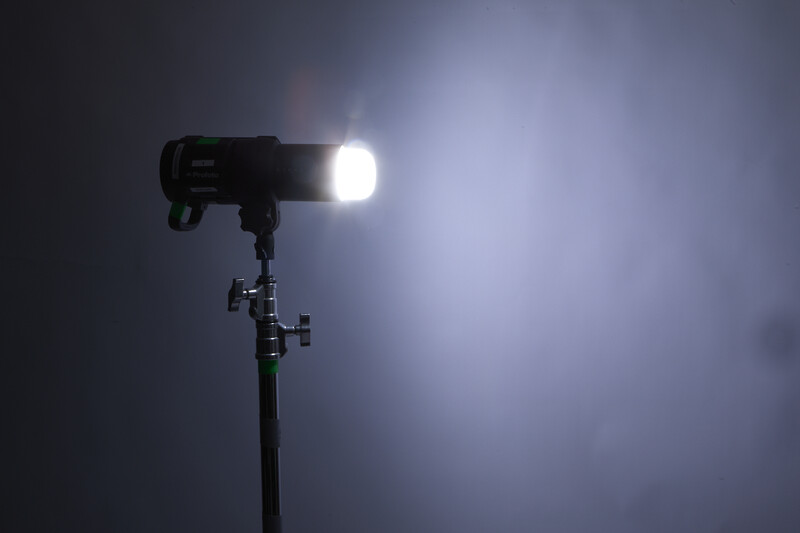 Professional spotlight mounted on adjustable stand with bright white beam against dark background.