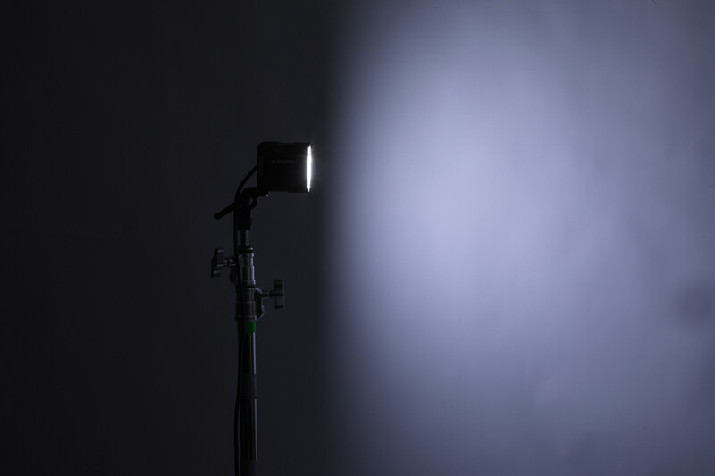 Studio light mounted on a stand against a dark backdrop, with bright beam illuminating a cloudy gray surface.