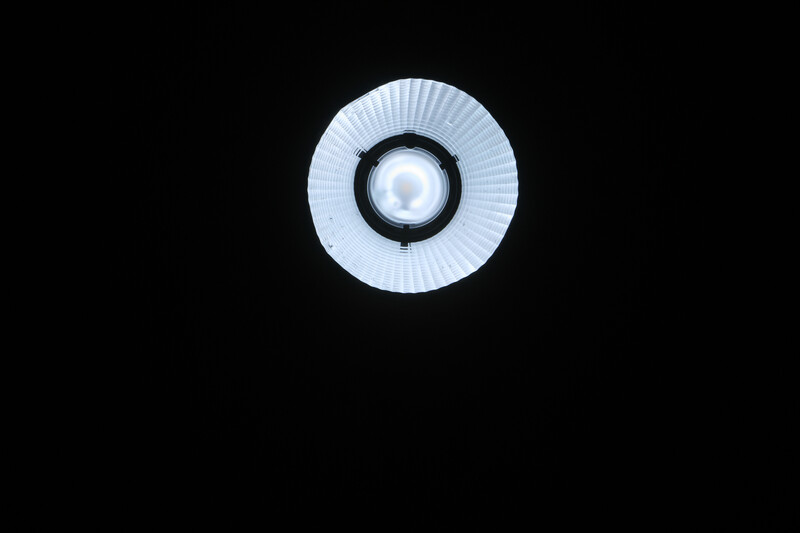 Overhead view of a circular LED ring light with white ribbed diffuser and black center against a dark background.