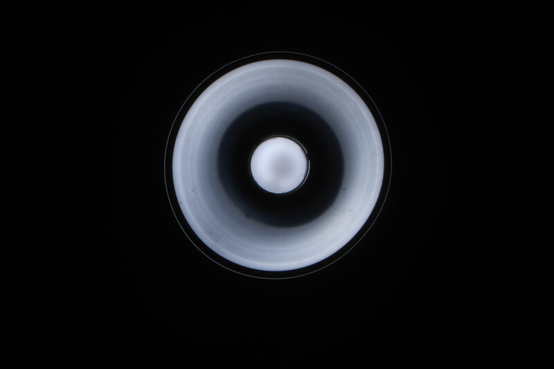 Close-up of a speaker cone with a white dome at center, shot from directly in front against a black background.