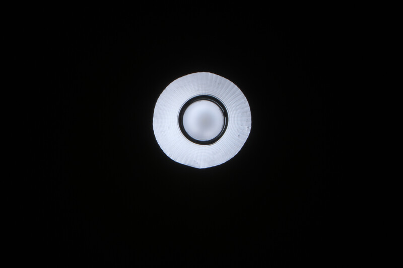 Close-up of a circular light modifier with concentric rings and a dark center aperture against black background.
