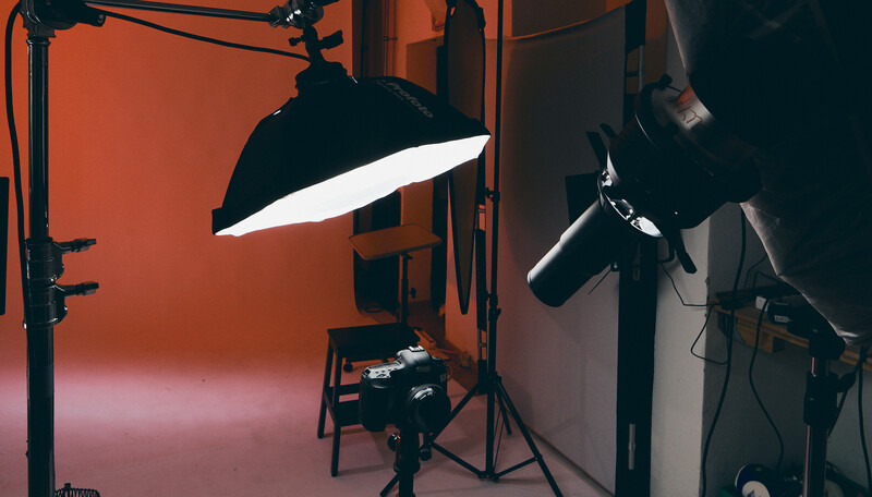Professional studio setup with orange backdrop, softbox key light, and fill light positioned for product or portrait photography.