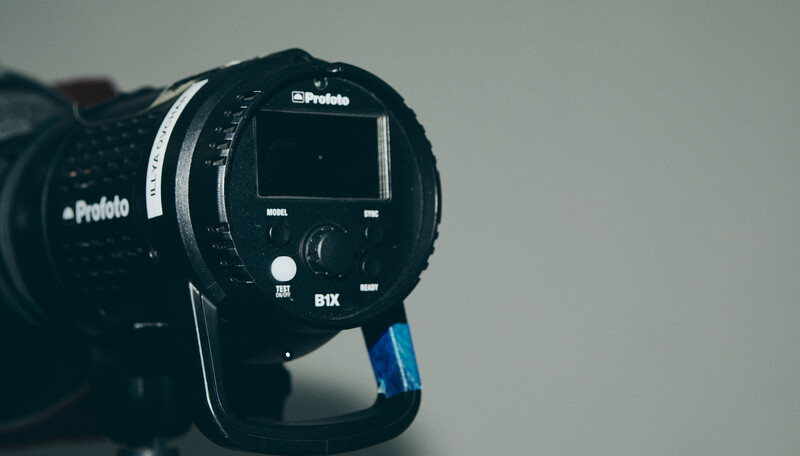 Profoto studio flash head with blue battery pack and control dial visible against neutral background.