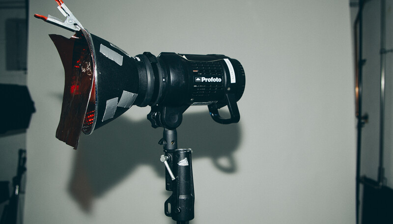 Profoto studio light mounted on stand with red reflector attachment and visible power cables.